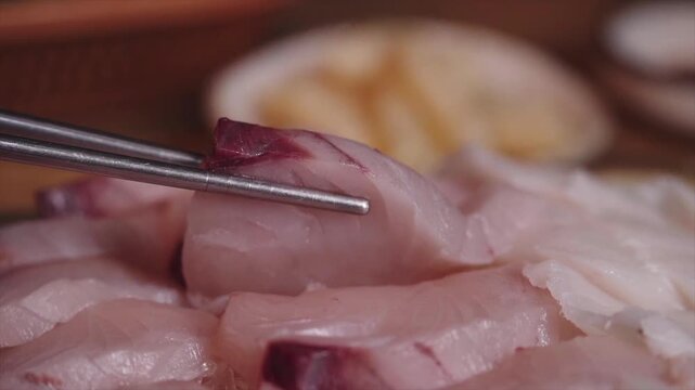 Lifting a piece of fresh Spanish mackerel sashimi with metal chopsticks