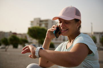 Obraz premium Smiling woman checking smartwatch while talking on phone during outdoor fitness break