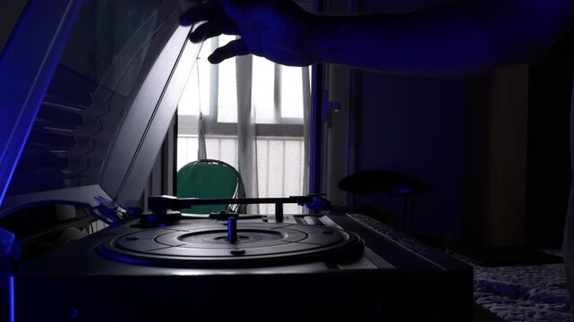 Adult man enjoying music from a vinyl record player while using a digital tablet in a cozy bedroom with natural window light. Lifestyle, relaxation and technology at home.