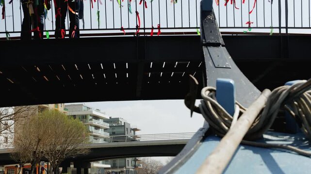 Immersive point-of-view shot from the bow of a traditional Moliceiro boat cruising through the city center canals of Aveiro, Portugal. The video features tourists walking near the famous bridges