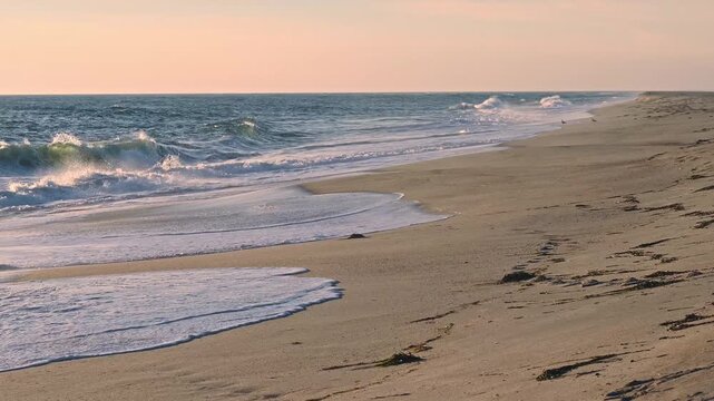 Gentle ocean waves roll onto the sandy beach as the warm golden light of the setting sun reflects beautifully across the water&rsquo;s surface
