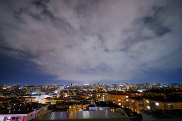 Fototapeta premium Clouds in the dark sky over cityscape with turkish apartment, residential buildings with warm lighting and illuminated windows in Istanbul, Turkey at night: wide angle