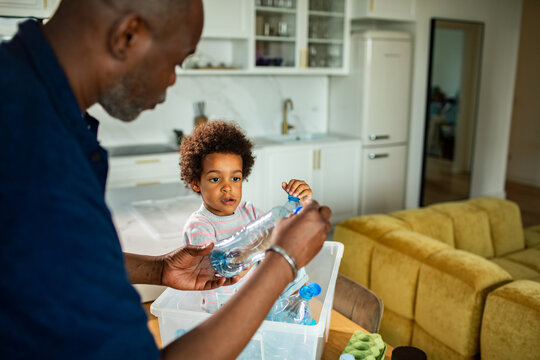 Father and toddler recycling plastic bottles in home kitchen