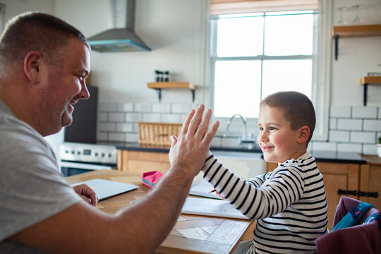 Father and son high five while doing homework at kitchen table