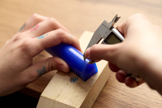 Close up of teenager hands measuring plastic tube with digital caliper on workbench, practicing technical skills and precision. Useful for STEM education, maker training, vocational learning
