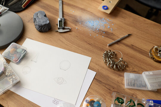 Overhead shot of jewelry designer workspace displaying sketching, measuring, sorting tools and ring sizers on desk, supporting product development, artisan branding, ecommerce content