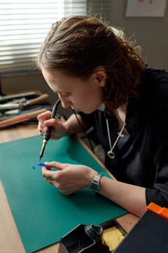 Vertical shot of young adult Caucasian woman soldering small plastic mold at workbench, crafting jewelry prototype with precision. Ideal for maker business, creative workshop concept