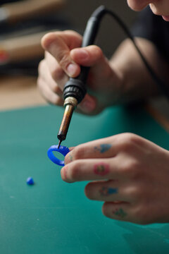 Vertical close up shot of female hands shaping blue plastic ring with soldering iron, practicing maker skills and product prototyping. Suitable for STEM education, DIY workshop, creative learning