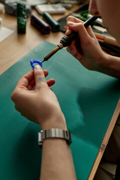 Vertical shot of young adult craftsperson soldering blue plastic model part at workbench, assembling prototype for product design or maker education content and DIY branding