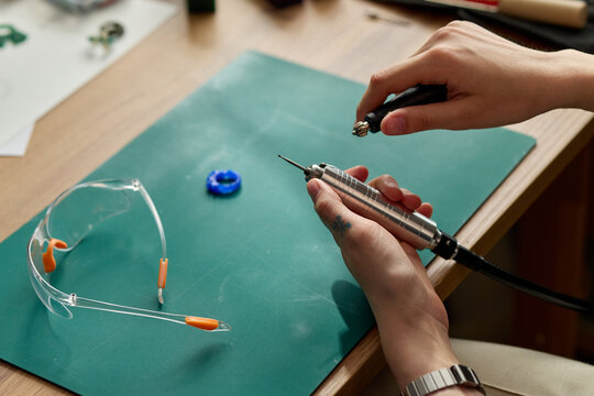 Close up of young adult artisan repairing rotary tool on workbench, handling precision parts near safety glasses. Ideal for engineering training, maker culture, repair service marketing