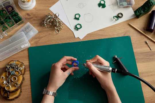 Close up of young adult craftsperson shaping ring prototype with rotary tool on workbench, developing jewelry design. Ideal for artisan branding, handmade product marketing, small business content