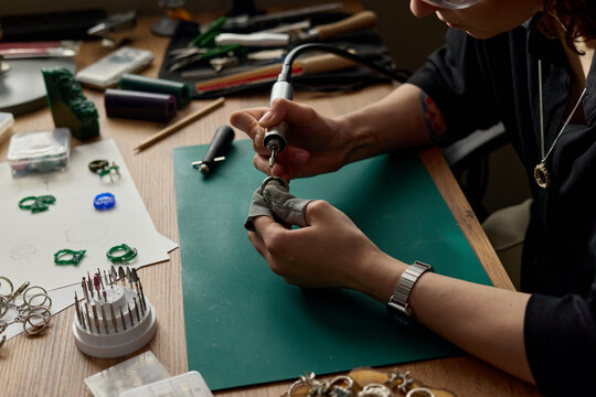 Close up of young adult woman polishing jewelry with rotary tool at workbench, crafting handmade accessories for small business production and artisan branding
