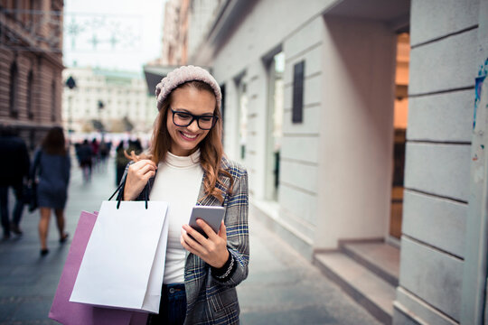 Young woman checks smartphone while shopping on city street
