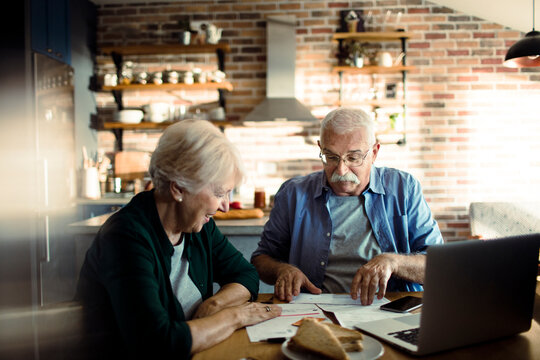 Senior couple paying bills with laptop at home kitchen table