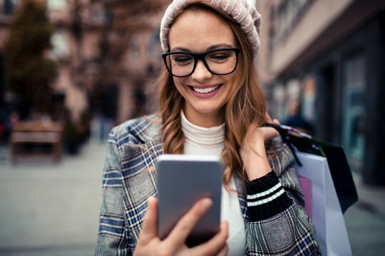 Smiling woman with shopping bags using smartphone on city street