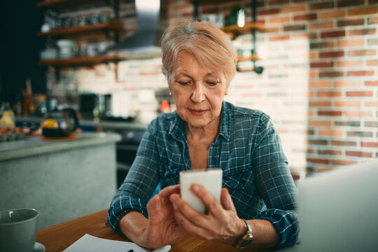 Senior woman using smartphone at home kitchen table