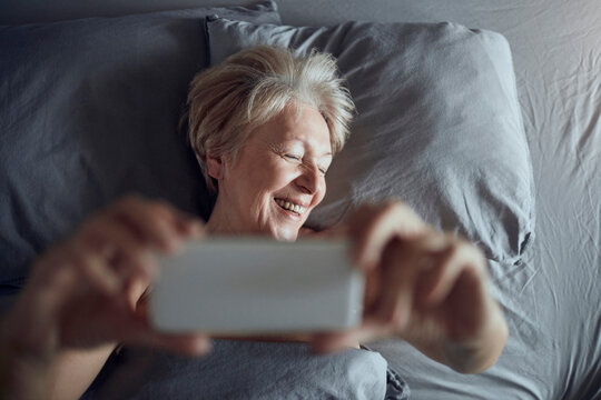 Smiling senior woman taking selfie in bed at home