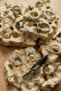 Vertical close up shot of handcrafted silver rings and pendants displayed on textured stone, presenting artisan jewelry collection, luxury accessory concept. Ideal for boutique branding and ecommerce