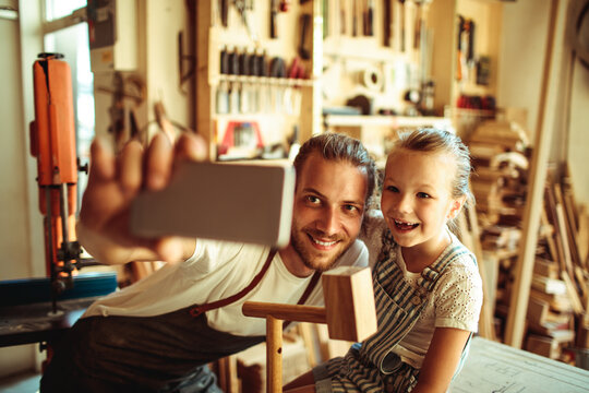 Father and daughter taking selfie in woodworking workshop