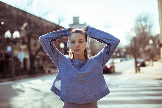 Young woman runner warming up with headphones on city street