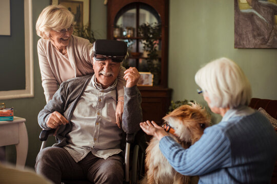 Senior man in wheelchair using vr headset at home with friends and dog