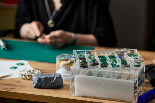 Close up of young adult woman crafting jewelry at workbench, arranging handmade plastic prototypes on organizer. Suitable for artisan business branding, ecommerce, craft workshop promotion