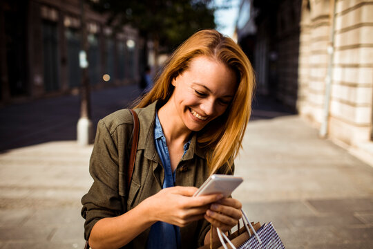 Smiling woman texting on smartphone while shopping downtown