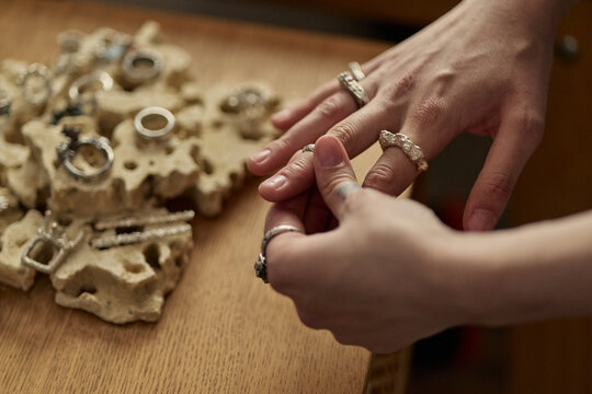 Close up of young adult woman trying on handmade rings while selecting jewelry from display, expressing accessory shopping and artisan retail concept. Ideal for boutique marketing