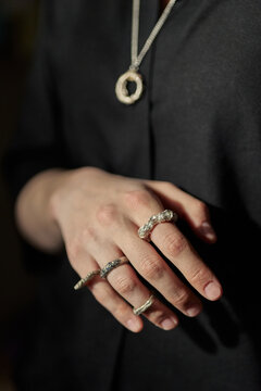 Vertical shot of young adult womans hand displaying multiple statement rings and pendant necklace, presenting artisan jewelry styling. Suitable for fashion retail, accessory branding