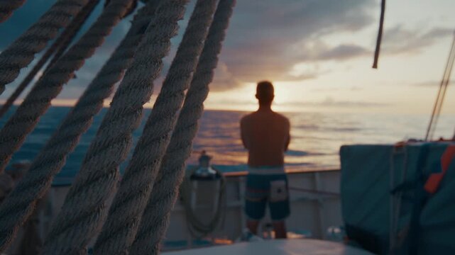 Sailing the Atlantic. Male sailor stands on the deck of the big sailing boat moving in the Atlantic Ocean under the sails and enjoys the last light of the day