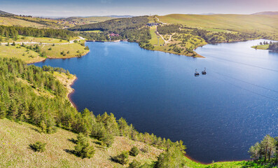 Zlatibor Ribnicko jezero reservoir with gondola cabins traversing over pine forests and hills, offering a beautiful natural landscape © EdNurg