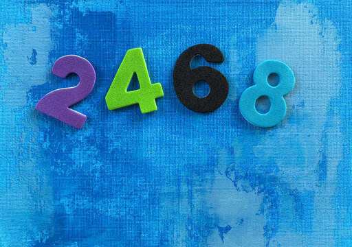 Colorful numbers 2, 4, 6 and 8 arranged on blue acrylic canvas background, representing even numbers, early math learning, preschool education, numeracy, counting practice, classroom activities.