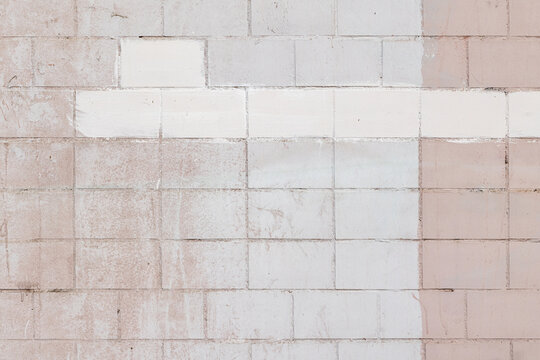 Faded pink and white painted cinderblock wall with visible texture, weathering and a horizontal white stripe. Minimal, neutral backdrop ideal for design, editorial, architecture, urban and background 
