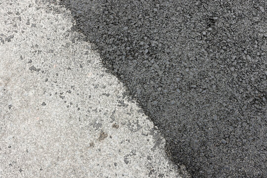 Closeup view of black asphalt overlay meeting aged concrete pavement, showing textured aggregate, contrast and surface detail typical of road repair, resurfacing projects and urban maintenance work