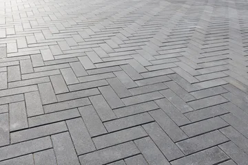 Gray concrete pavers forming a clean Herringbone geometric pattern of an outdoor walkway. Close-up view emphasizes texture, repetition and modern design for urban pathways. Selective focus © evannovostro