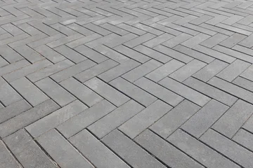 Herringbone pattern of gray concrete pavers forming a clean, geometric outdoor walkway. Close-up view emphasizes texture, repetition and modern hardscape design for urban pathways © evannovostro