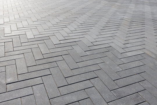 Gray concrete pavers forming a clean Herringbone geometric pattern of an outdoor walkway. Close-up view emphasizes texture, repetition and modern design for urban pathways. Selective focus
