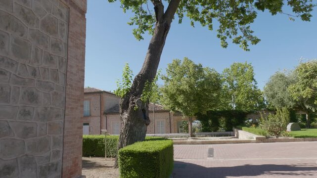 A tracking shot revealing a beautiful garden with a courtyard, manicured hedges, lush trees, tall palm trees, and traditional stone palatial buildings under a bright, sunny sky. Ideal for concepts rel