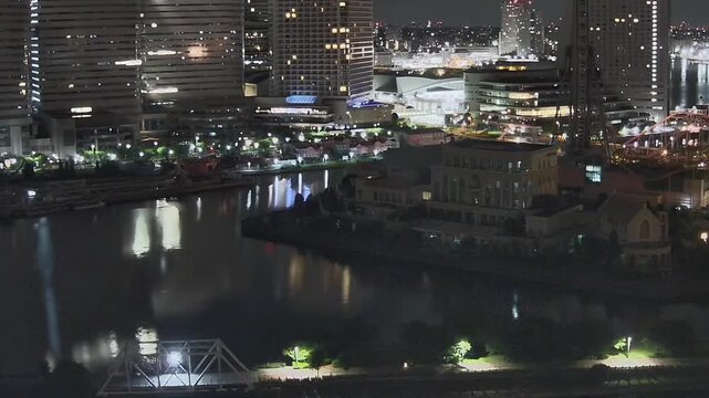 Timelapse of illuminated skyscrapers and waterfront reflections at night in Yokohama, Japan. Urban cityscape with bridges and harbor lights.