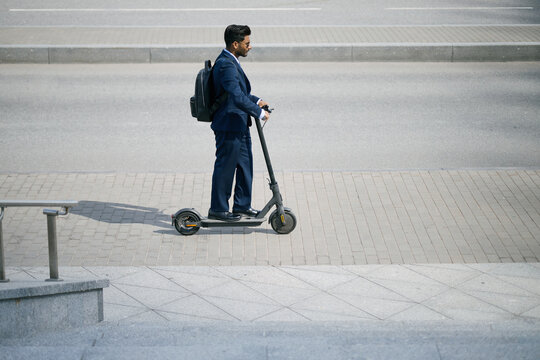 Indian businessman riding electric scooter during urban commute, carrying backpack and moving to work. Ideal for business mobility, sustainable transport, modern commuting campaigns