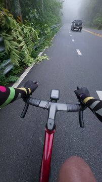 First-person point of view of a road cyclist riding along a foggy mountain road after rainfall through lush tropical forest. The immersive footage captures misty weather, wet pavement, scenic landscap
