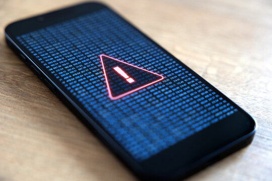 Smart phone screen shows system warning sign, computer crime, system hacked. Network security, firewall, samrtphone virus, data, privacy, safety, danger, data breach, computer problems.