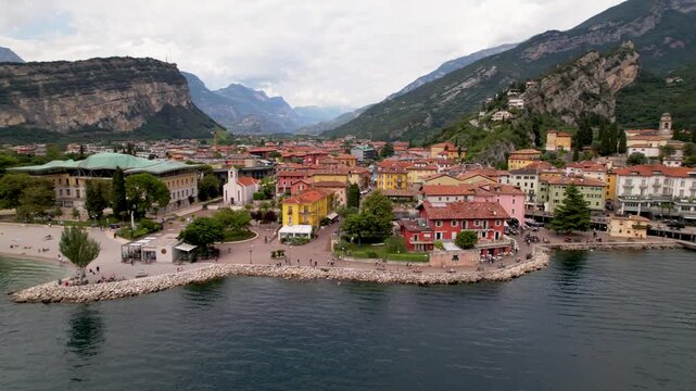 Aerial drone side view over Torbole on Lake Garda in Italy with colorful pastel houses beaches and Arco castle on cliff in background. Scenic alpine lake landscape in sunny 4K stock video