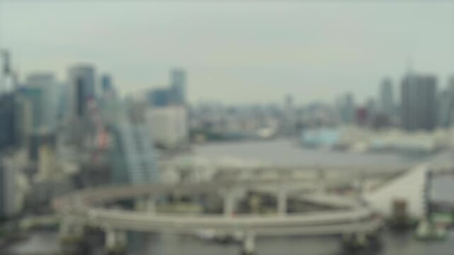 Soft focus timelapse of an elevated expressway loop over a river in Tokyo Japan with city skyline in the background. Abstract urban traffic and infrastructure scene.