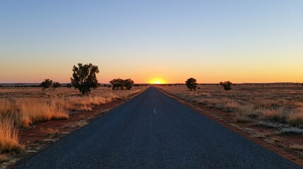 Naklejka premium Endless asphalt road stretches toward a brilliant sunset in vast, dry wilderness
