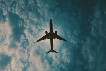 Fototapeta premium Commercial Airplane Flying Overhead Against Dramatic Blue Cloudy Sky — Travel and Aviation Concept