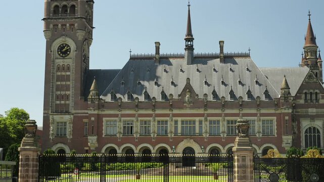 An ornate palace facade features a tall clock tower and wrought iron fence under a clear summer sky.