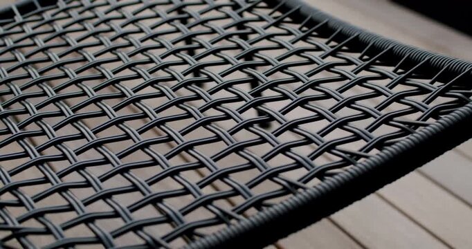 Close-up of a black wicker chair. The focus is on the woven pattern of the seat. Ideal for home decor, interior design, or furniture-related projects. Its modern style and comfortable texture