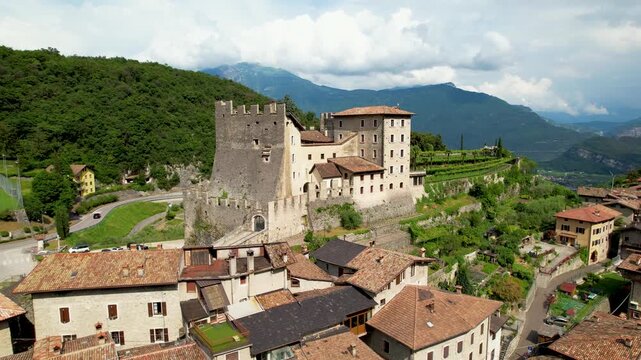 Tenno castle Italy 4k drone pullaway orbit view of medieval hilltop borgo town. Aerial reveal panorama of Lake Garda and Alps mountains background green valley