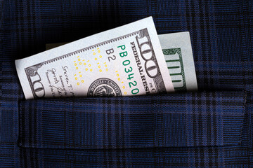 Closeup of a $100 US dollar bill tucked into a blue plaid suit pocket, symbolizing finance, success, and wealth. © alesmunt
